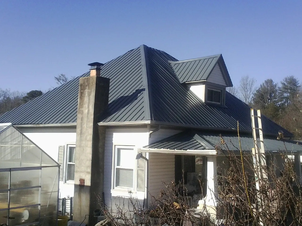 Dark blue standing seam metal roof on a white farmhouse with dormer — Slate & Tile Roof Repair by Roofing Brothers in Intervale