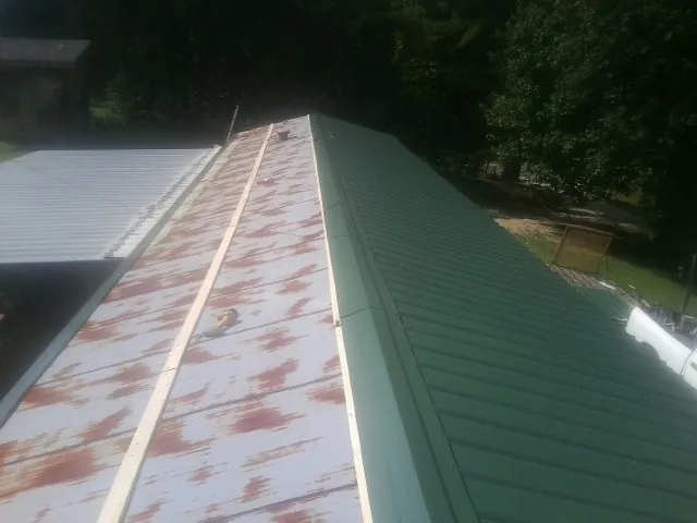 Old rusted panels beside newly installed green metal roofing — Wind Damage Roof Repair by Roofing Brothers in Intervale