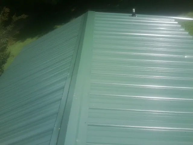 New green metal panels meeting at the ridge of a roof — Flat Roof Repair work by our crew in Intervale