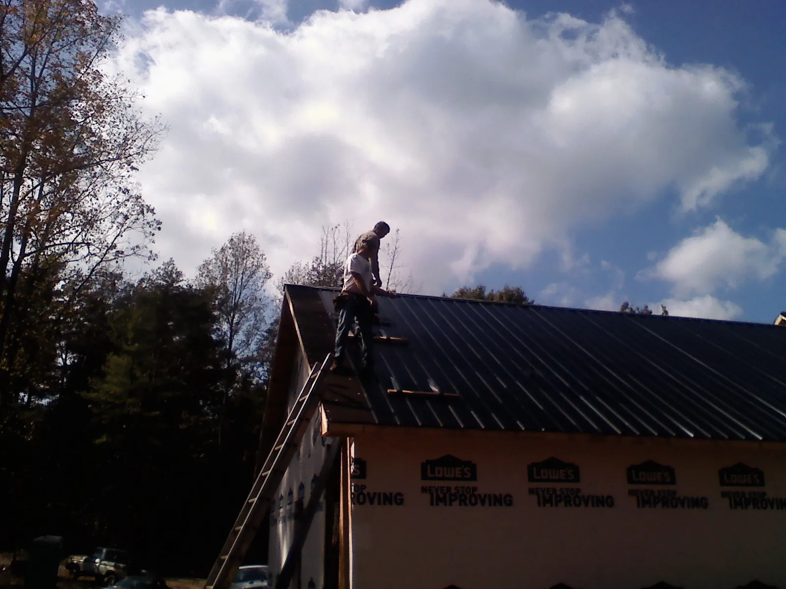 Roofer fastening dark metal panels high against a cloudy sky, from a Roof Inspection job in Intervale